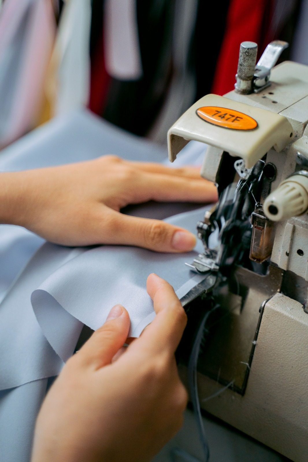 Hands guiding light fabric through an industrial overlock machine