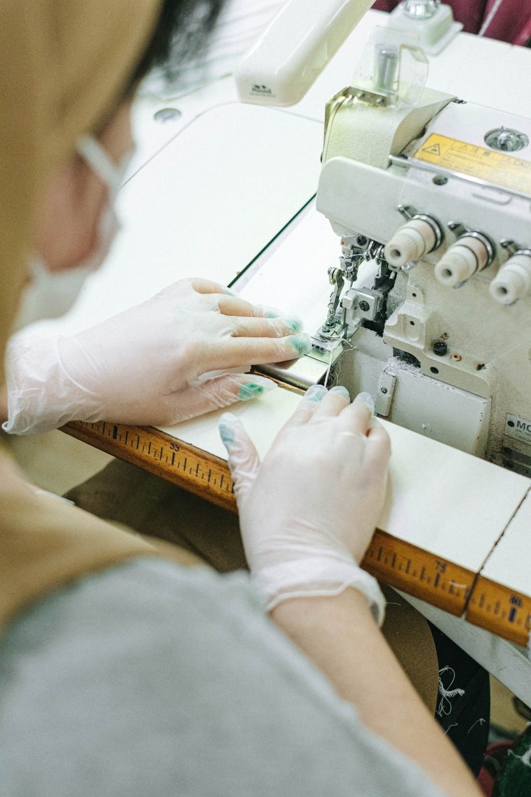 A machinist guiding fabric through an industrial overlock machine, gloved hands at the needle