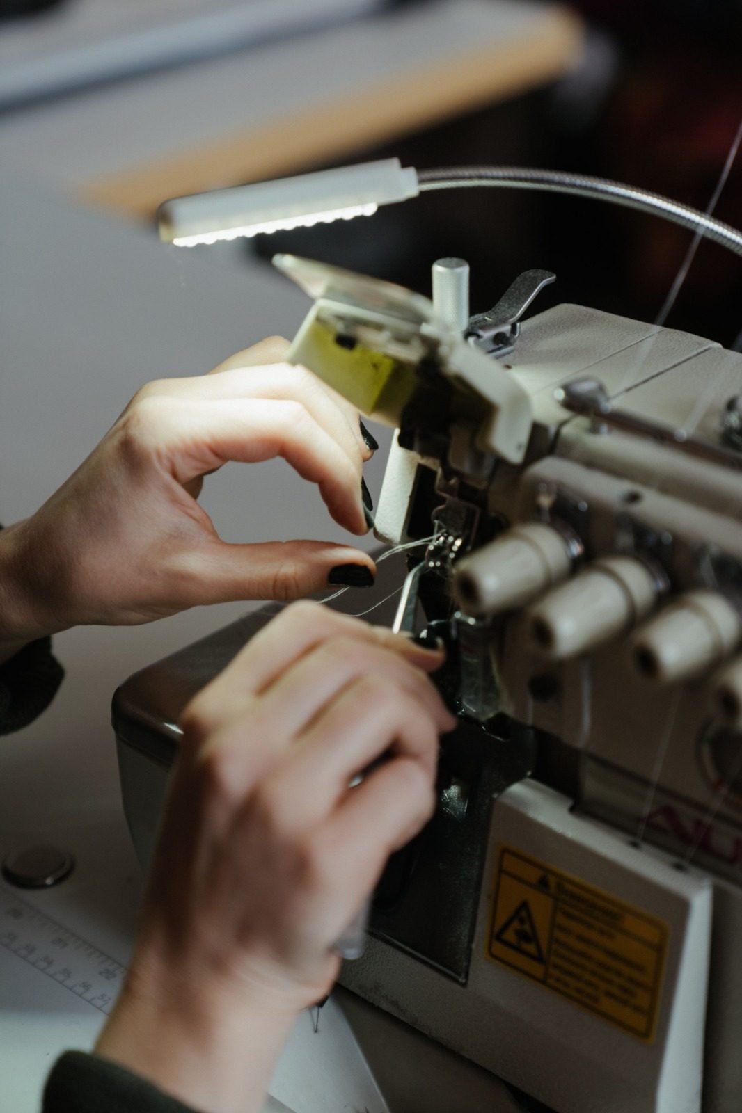 Hands threading an industrial overlock machine under a work lamp