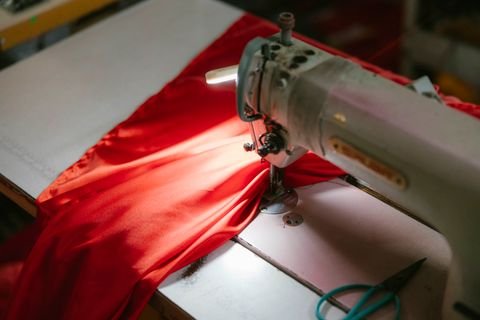 An industrial sewing machine stitching red fabric, close up